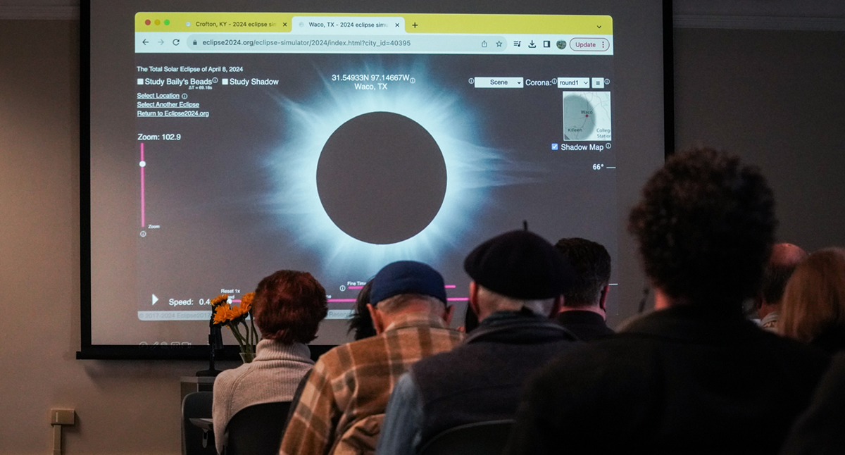 guests listen to a speaker with a photo of an eclipse on a big screen